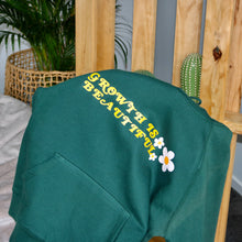 Load image into Gallery viewer, Bottle green hoodie with flower prints and quote and a palm tree and bean back in the background 

